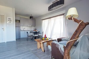 Una cocina moderna con armarios grises, una zona de comedor con mesa de madera y una sala de estar con sofá y lámpara.