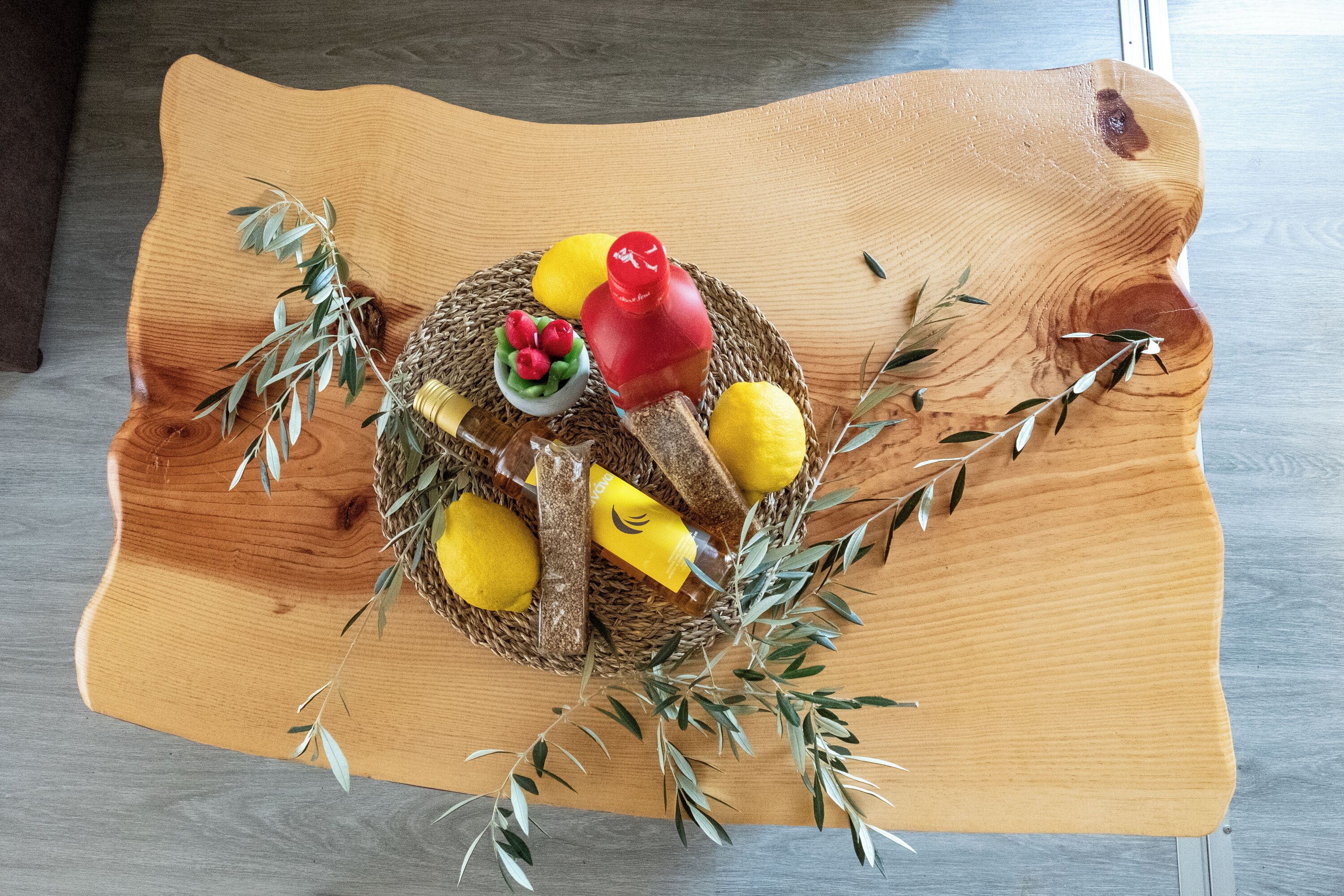 A wooden table with a woven basket containing lemons, a red bottle, and a small bowl of red berries.