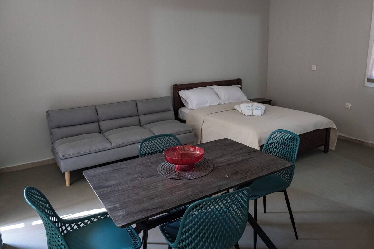 Et værelse med seng, sofa, spisebord med stole og en rød skål på bordet.