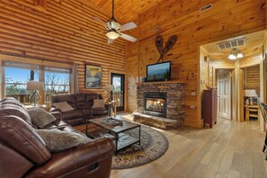 L’intérieur d’une cabane en rondins, avec une cheminée, un canapé en cuir et un ventilateur de plafond.