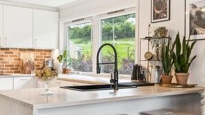 Een keuken met een groot raam, een spoelbak en diverse keukenbenodigdheden.