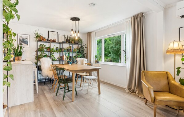 A dining area with a wooden table and chairs, surrounded by shelves with plants and books.