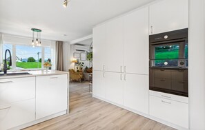 A modern kitchen with white cabinetry, a built-in oven, and a view of a green landscape through the window.