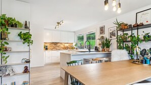 Een moderne keuken met witte kasten, een houten eettafel en verschillende planten.