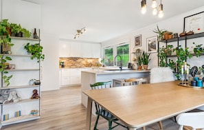 A modern kitchen with white cabinets, a wooden dining table, and various plants. - Awesome apartment in Strandebarm (Strandebarm)
