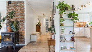 Een woonkamer met een metselwerk open haard, houten vloeren, een witte bank en een plankensysteem vol planten.