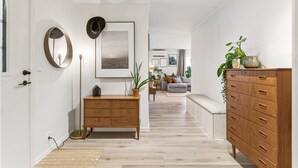 Een gang met een houten dressoir, een spiegel, een ingelijst kunstwerk en een plant.