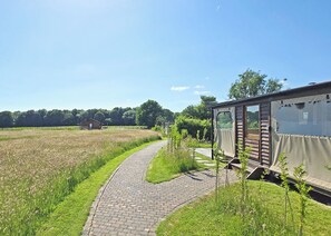 A rural setting with a paved path leading to a mobile home-like structure with a covered porch.