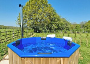 A wooden hot tub with a blue interior, surrounded by a wooden fence and a large tree.
