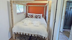 Een bed met hemel en witte lakens en kussens, een vloerkleed met zebraprint en een houten vloer.