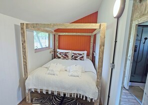 A four-poster bed with white linens and pillows, a zebra-patterned rug, and a wooden floor.