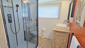 A bathroom with a glass-enclosed shower, a sink with a wooden vanity, and a window with blinds.