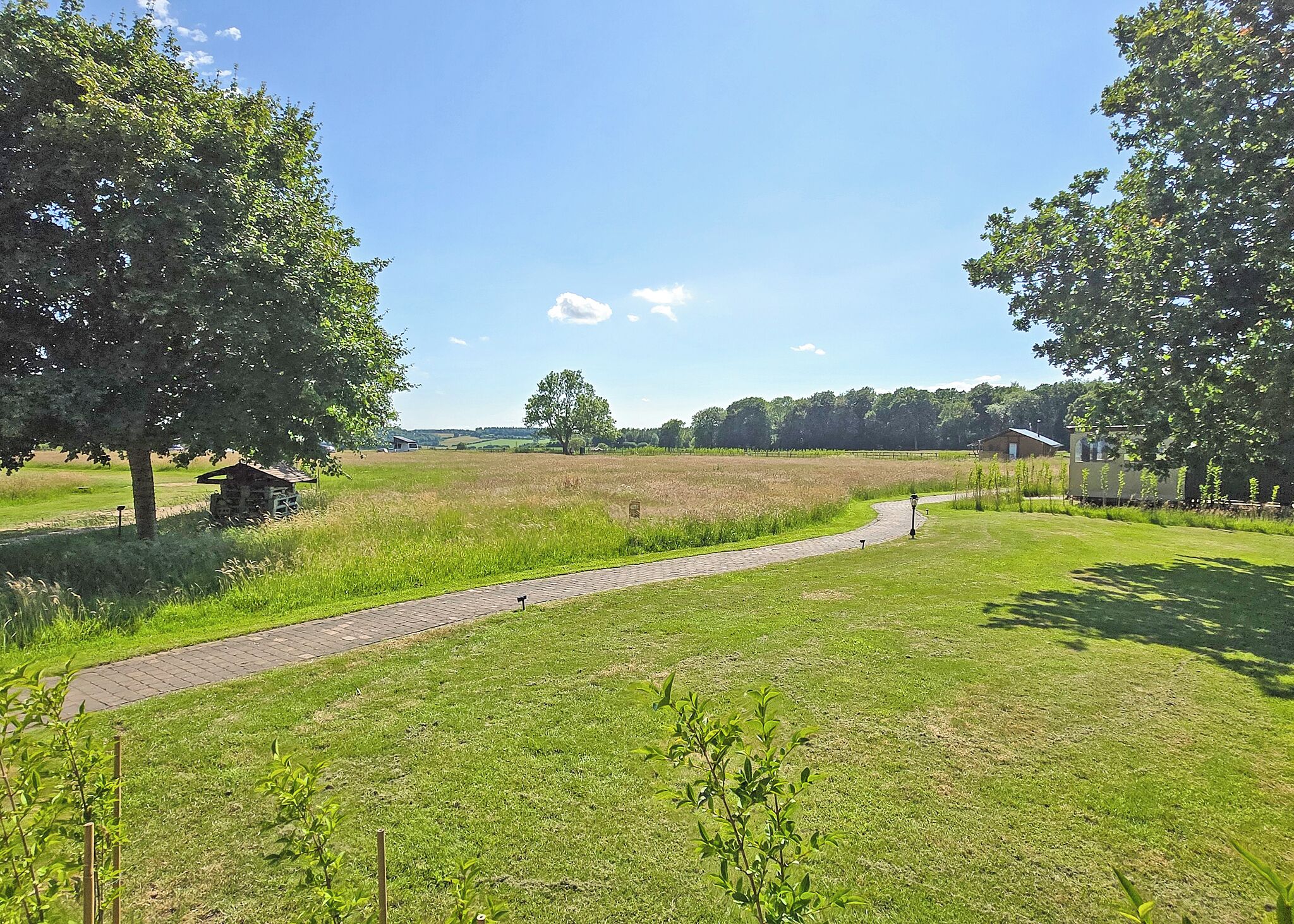 A rural landscape with a paved path, trees, and a small structure.