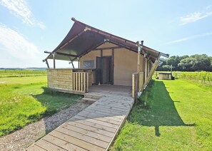 A small, single-story building with a sloped roof, a wooden deck leading to the entrance, and a grassy field in the background.