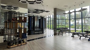 A gym with weightlifting equipment, a punching bag, and a large window offering a view of the outdoors. - Căn hộ The Oceanfront tại Cam Ranh (The Oceanfront Apartment At Cam Ranh) (Cam Lâm)