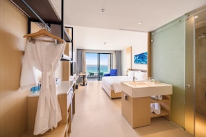 Ein Hotelzimmer mit Bett, Badezimmer mit Waschbecken und Spiegel, einem Bademantel, der auf einem Gestell hängt, und Meerblick durch das Fenster.