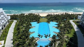 A resort with a central swimming pool, palm trees, and a beach view. - Căn hộ The Oceanfront tại Cam Ranh (The Oceanfront Apartment At Cam Ranh) (Cam Lâm)