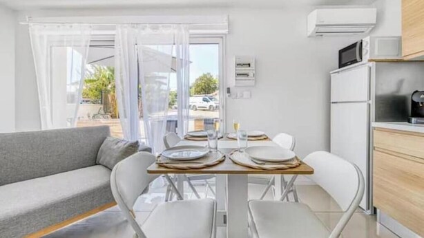 Une cuisine moderne avec des appareils électroménagers blancs, un coin repas avec une table dressée pour deux personnes et un canapé gris.