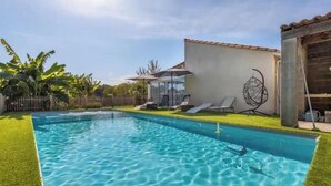 Une piscine à l’eau claire, entourée d’une pelouse et d’un petit bâtiment doté d’un toit en tuiles.