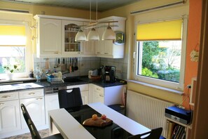 Une cuisine avec des meubles blancs, un plan de travail noir, une machine à café et une fenêtre avec des stores.