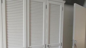 A white wardrobe with horizontal slats, a door with a keyhole, and a dark object on the wall. - VENTO DI BOLINA (Giovinazzo)