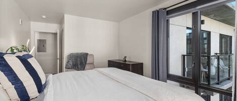 Una habitación de hotel moderna con una cama grande, un escritorio pequeño, una silla y un balcón con barandilla de cristal.