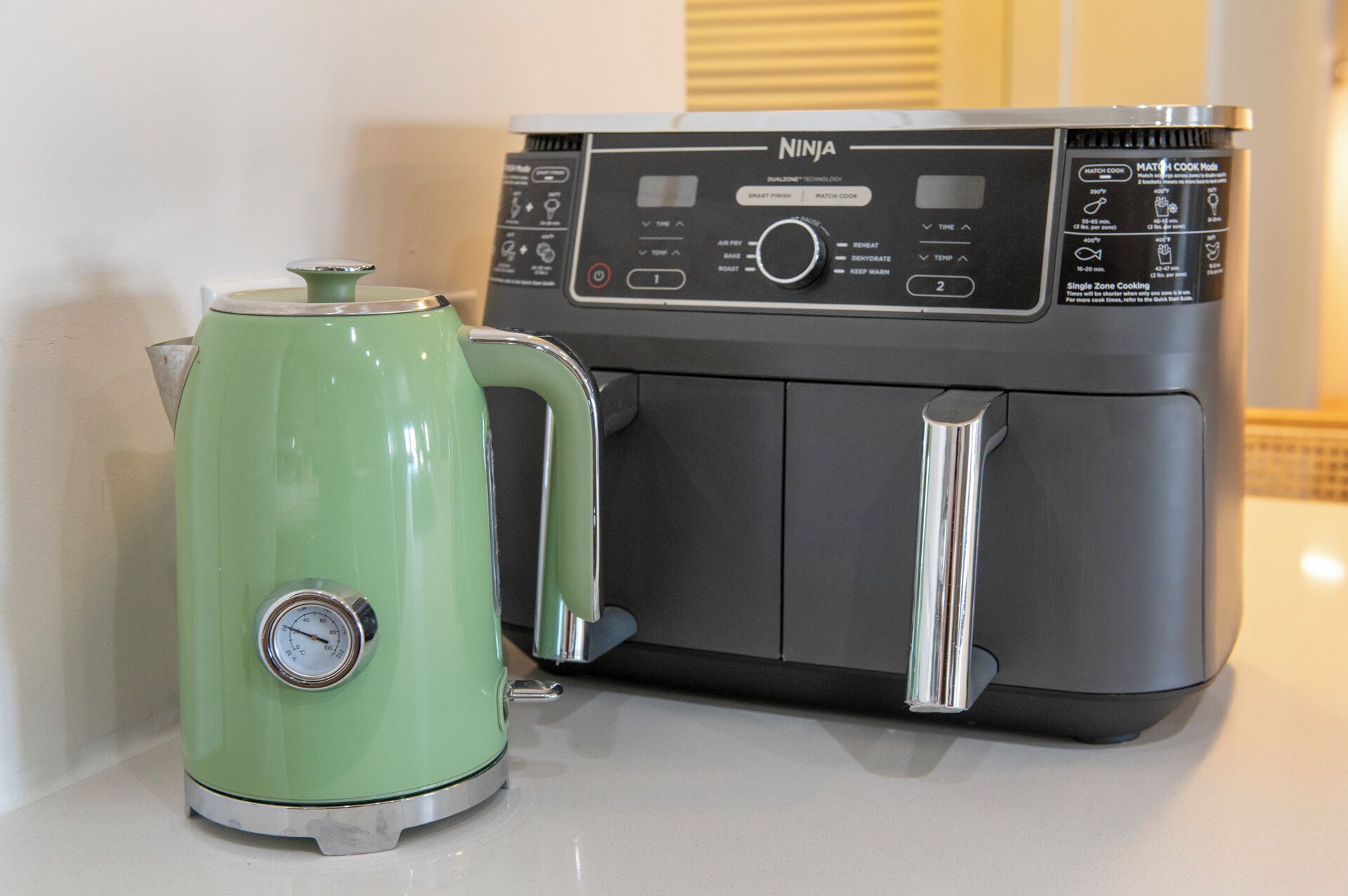 A kitchen with a green kettle and a black Ninja air fryer.