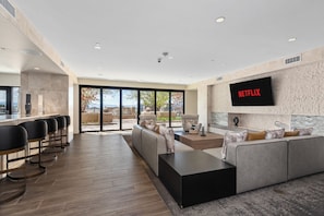 Un grand espace de vie comprenant un grand écran de télévision, un canapé, une table basse et un coin bar avec des chaises.