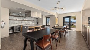 Cozinha moderna com uma ilha grande, área de jantar com uma mesa comprida e cadeiras, e vista para um pátio externo através de uma porta de vidro.