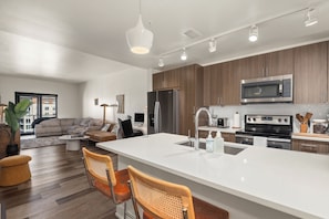 Une cuisine moderne dotée d’un îlot central, d’appareils électroménagers en acier inoxydable et de meubles de rangement en bois.