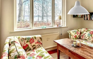 A cozy room with a wooden table, two floral-patterned chairs, a radiator, and a window with a view of trees. - Beautiful home in Sjöbo with lake view (Sjöbo)