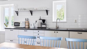 Ett modernt kök med vita skåp, en svart bänkskiva, en kaffebryggare, en vattenkokare och en mikrovågsugn. Vid bordet står två blå stolar.