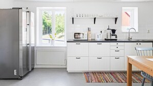 Ett modernt kök med vita skåp, ett kylskåp i rostfritt stål, en mikrovågsugn, en kaffebryggare och ett fönster med utsikt över grönområden.