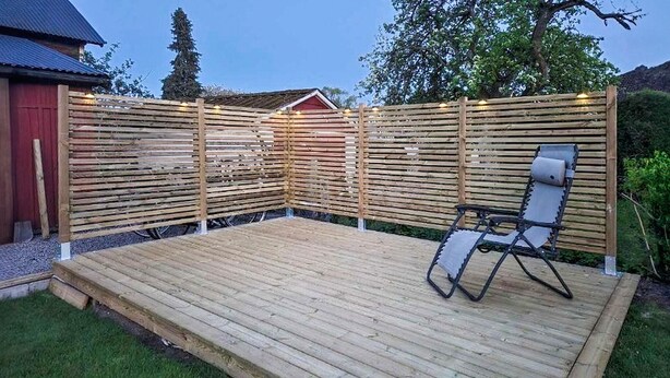 Ett trädäck med en enda solstol, omgivet av ett trästaket med ljusslingor.