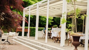 Un patio al aire libre con mobiliario blanco, una pérgola y una planta en maceta.
