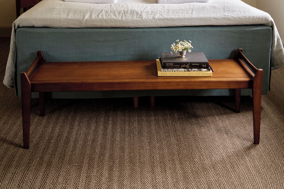 A neatly made bed with pillows, a bedside lamp, and a small table with books.