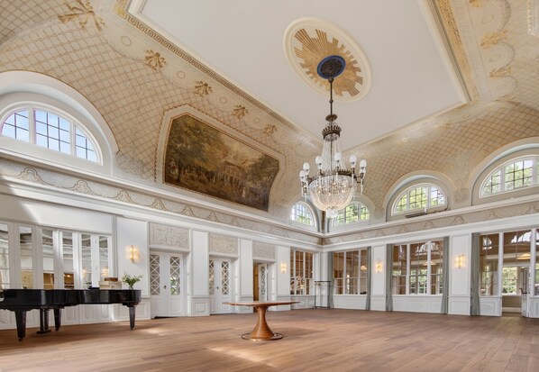 Un vaste hall agrĂ©mentĂ© dâun piano, dâune table centrale et dâun grand lustre.