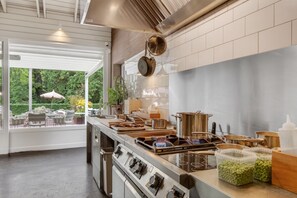 Une cuisine moderne dotĂ©e dâappareils Ă©lectromĂ©nagers en acier inoxydable, dâun grand Ăźlot central et offrant une vue sur lâextĂ©rieur.