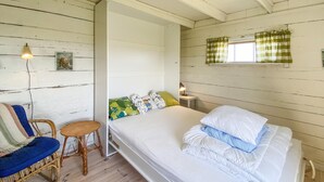 Ett rum med en säng, en stol, ett litet bord och ett fönster med gardiner.