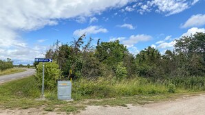 Ett vägskylt som visar vägen till Badplats, ett grönområde vid vägkanten med tät vegetation, och en elcentral märkt med texten ”Kabeljon”.