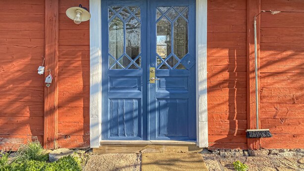 Ett rött trähus med en blå dubbeldörr, en lampa och en liten brevlåda.