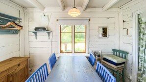 Ett rum med ett matbord i trä, blå stolar, en bänk, en radio och ett fönster med utsikt över grönområden.