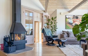 A cozy living room with a wood-burning stove, a comfortable sofa, a chair, and a large plant. - Amazing home in Visby (Visby)