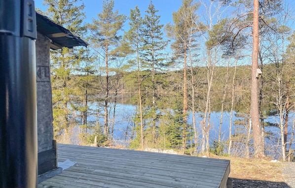 A wooden deck overlooking a lake with tall trees in the background.