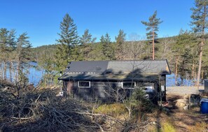 A cabin with a dark roof, surrounded by trees and a body of water.
