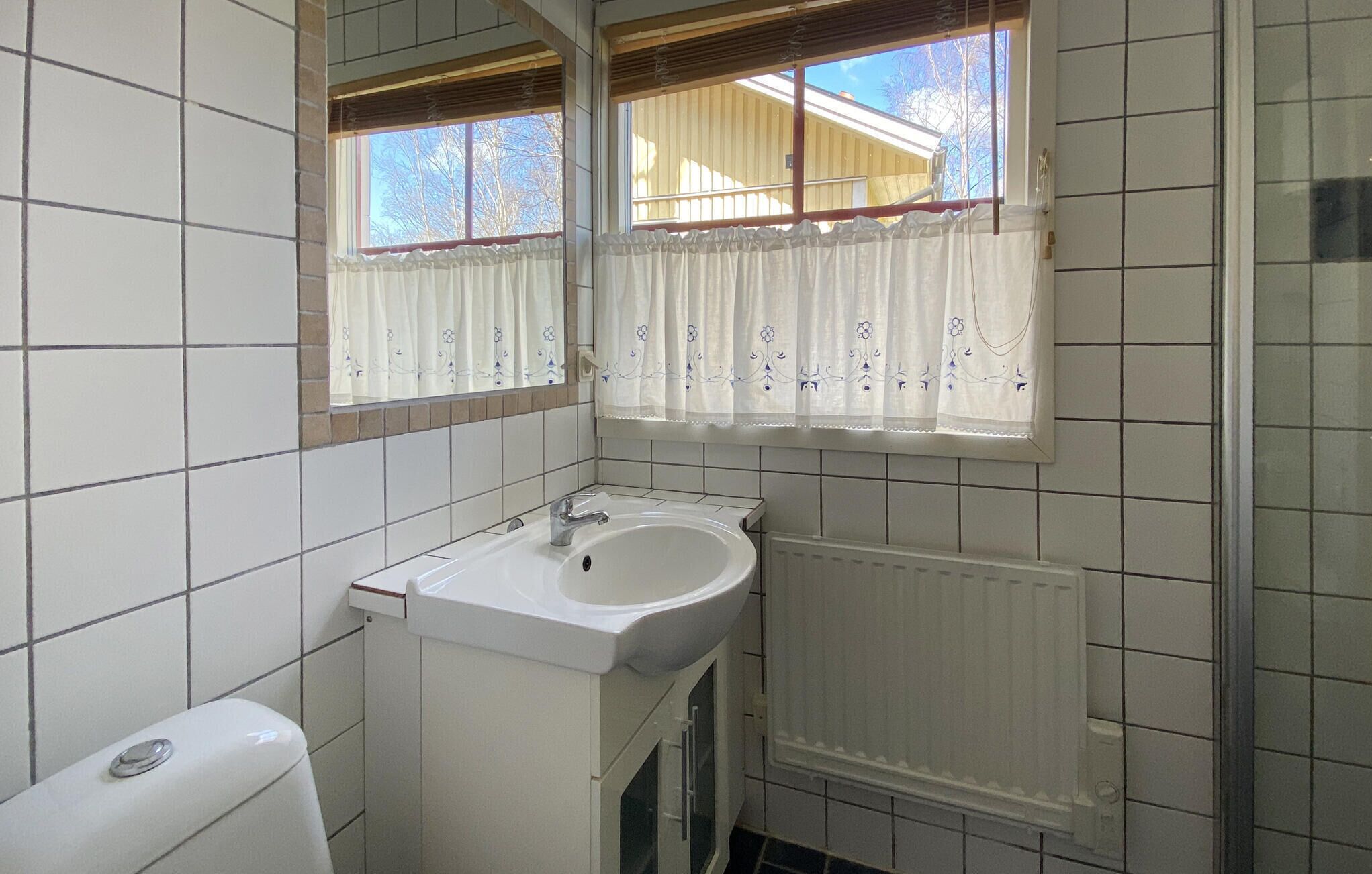 A bathroom with a white sink, a toilet, a window with curtains, and a radiator.