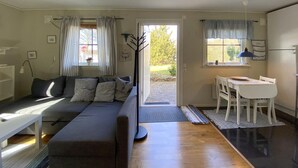 En kompakt opholdsstue med sofa, spisebord og dør til et udendørs område.