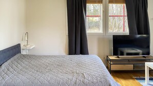 Et soveværelse med seng, fjernsyn, sengebord og et vindue med gardiner.