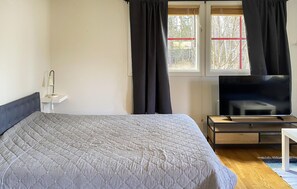 A bedroom with a bed, a TV, a bedside table, and a window with curtains. - 1 bedroom cozy home in Färjestaden (Färjestaden)