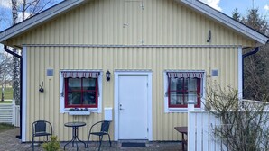 En toetagers bygning med en hvid dør, to vinduer med røde rammer, og en lille veranda med et bord og to stole.